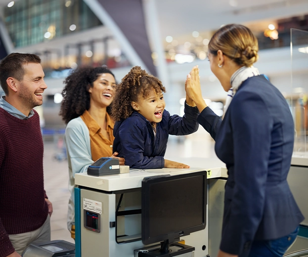An airport check-in counter agent giving a high five to a smiling young girl traveling with her family, showcasing proactive communication and trust in OTA customer support.