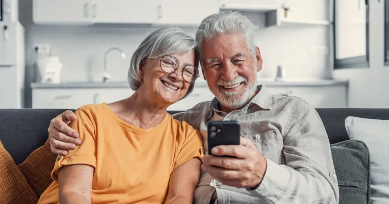 Senior couple smiling at a phone together at home