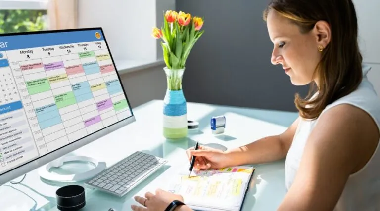 Woman taking notes beside a monitor showing a scheduling calendar