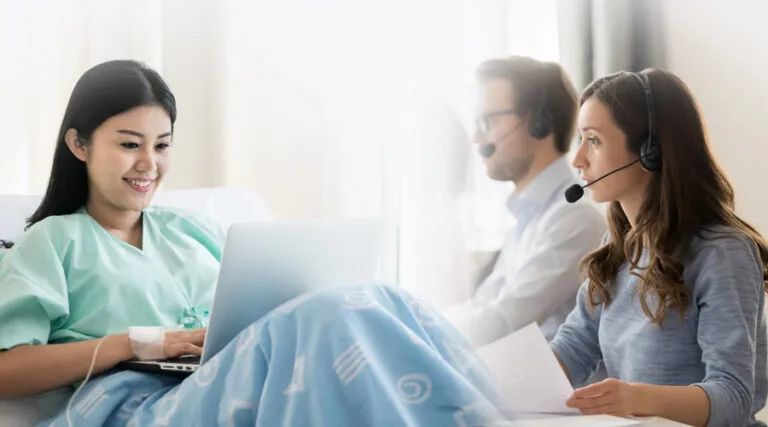 Patient on a laptop in bed while agents in headsets take calls