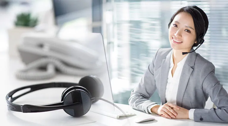 Smiling agent in a headset at her desk with a headset in the foreground