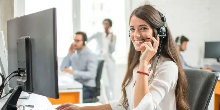 Smiling retail support agent in a headset on a busy contact center floor