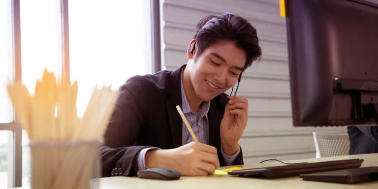 Order processing agent on the phone taking notes at his desk